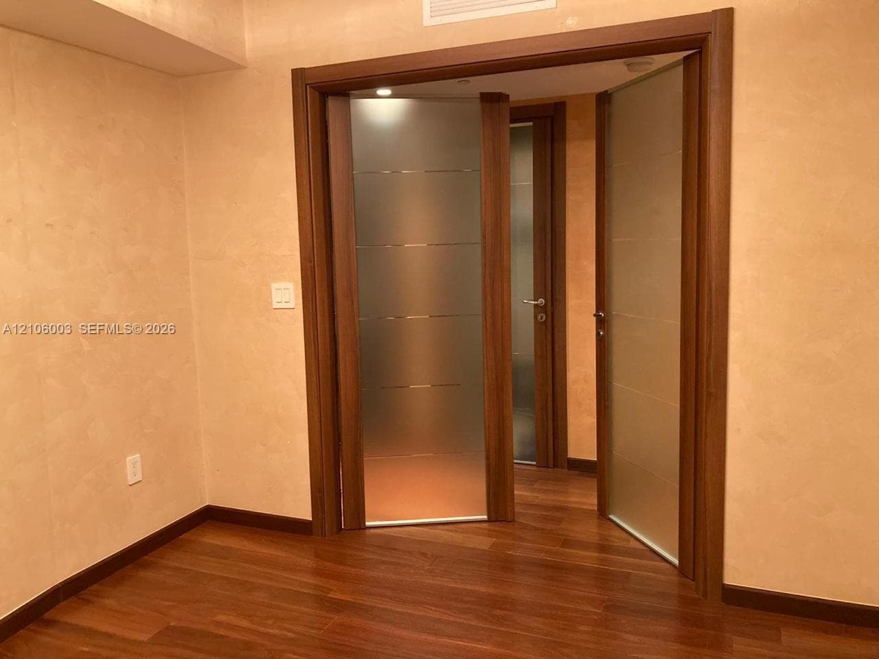 Wood-finish flooring, textured wall finish, and wood-framed doors with frosted glass inserts and horizontal metal accents