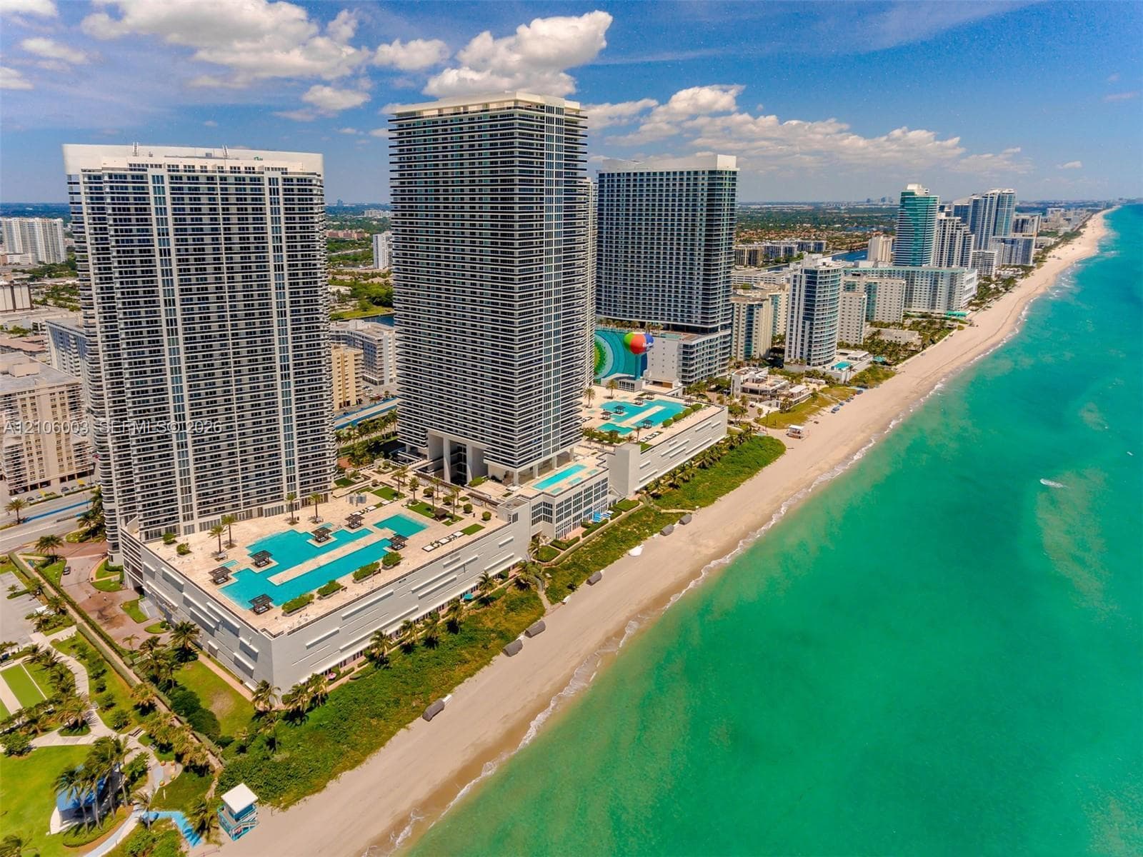 High-rise residential towers featuring oceanfront positioning, multiple tiered swimming pools, sun decks, and direct beach access