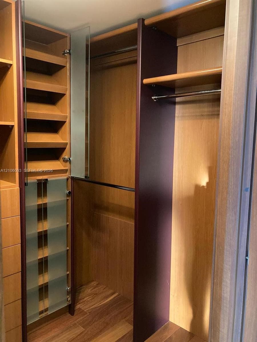 Custom closet featuring wood-finish cabinetry, built-in shelving, frosted glass door panels, integrated hanging rods, and wood-finish flooring