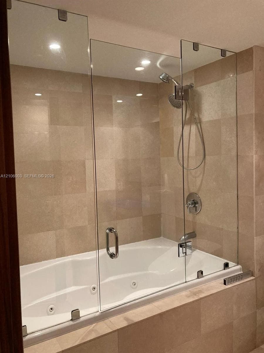 Jetted soaking tub with tile surround, frameless glass panel, and adjustable handheld shower fixture