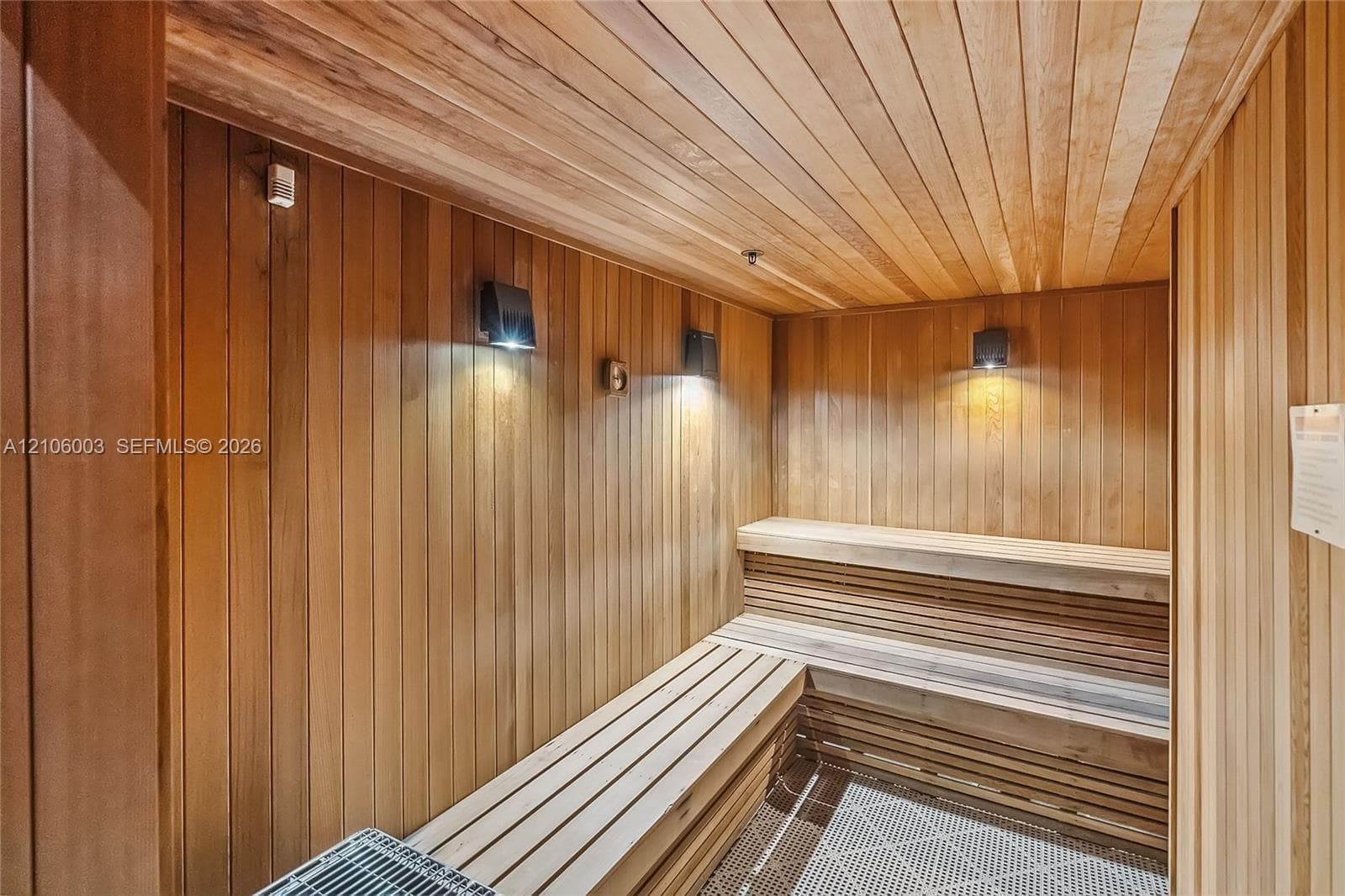 Sauna featuring tongue-and-groove wood paneling, multi-level built-in bench seating, and wall-mounted lighting