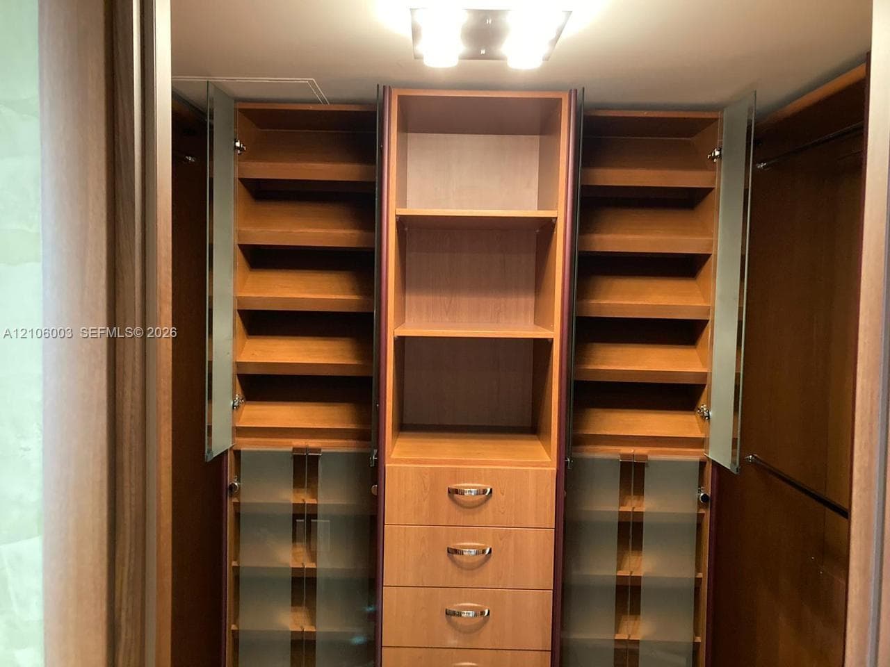 Custom built-in wood-finish closet storage system featuring adjustable shelving, integrated drawers with metallic pulls, frosted glass cabinet doors, and recessed ceiling lighting