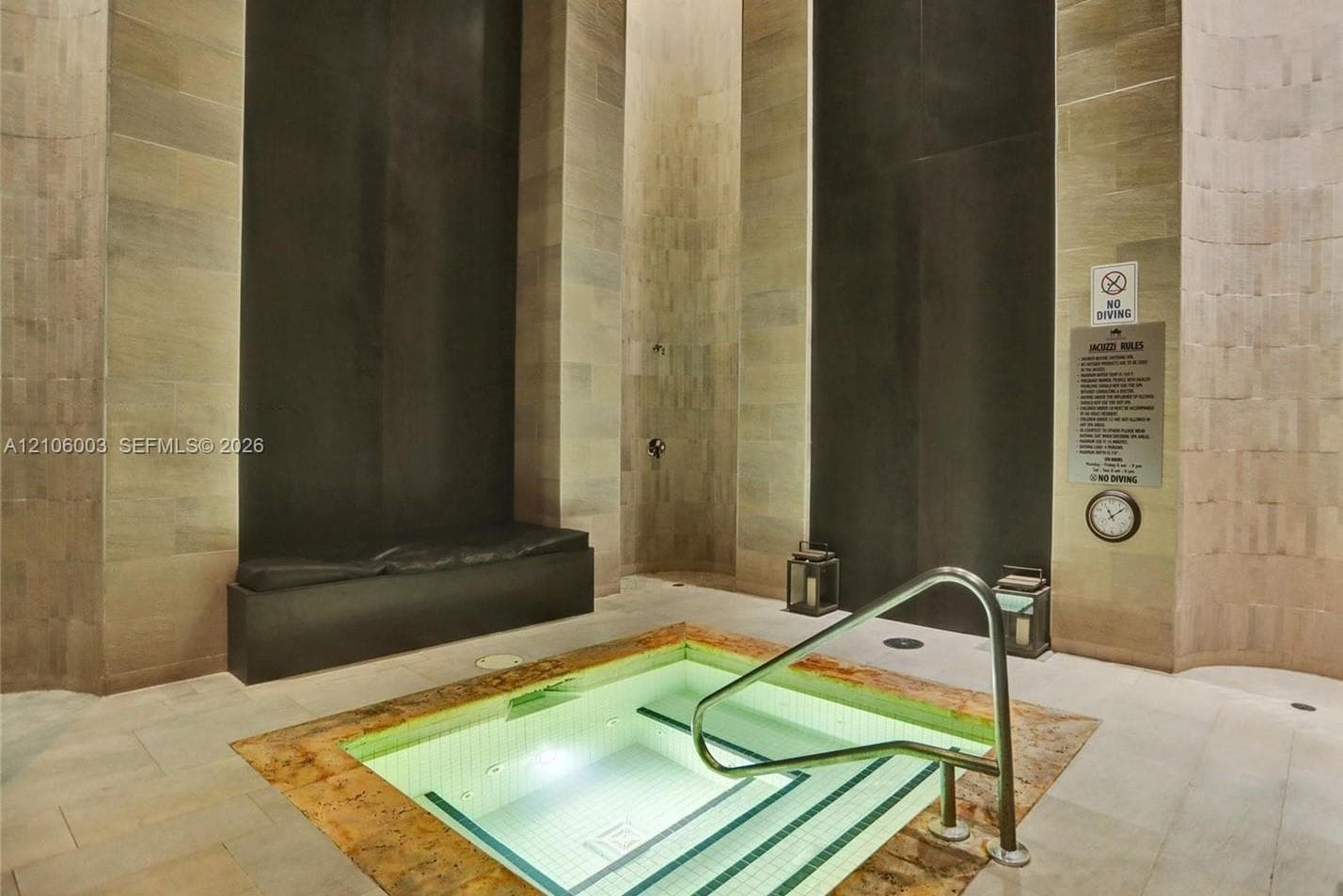 Indoor hydrotherapy pool featuring stone tile flooring, vertical stone wall accents, integrated bench seating, and a metal handrail