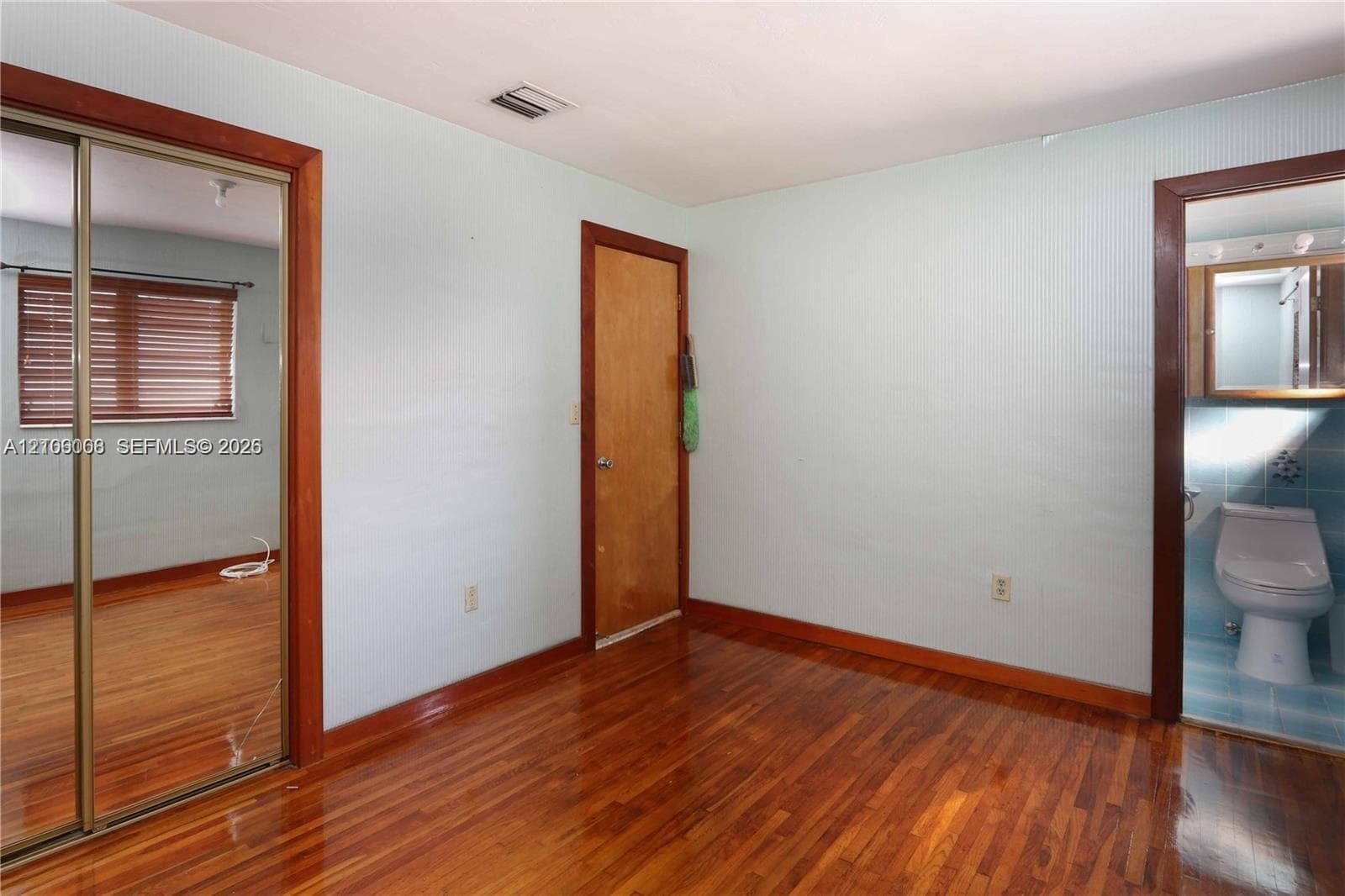 Wood-finish flooring, full-length sliding mirror closet doors, and interior wood-trimmed door frames