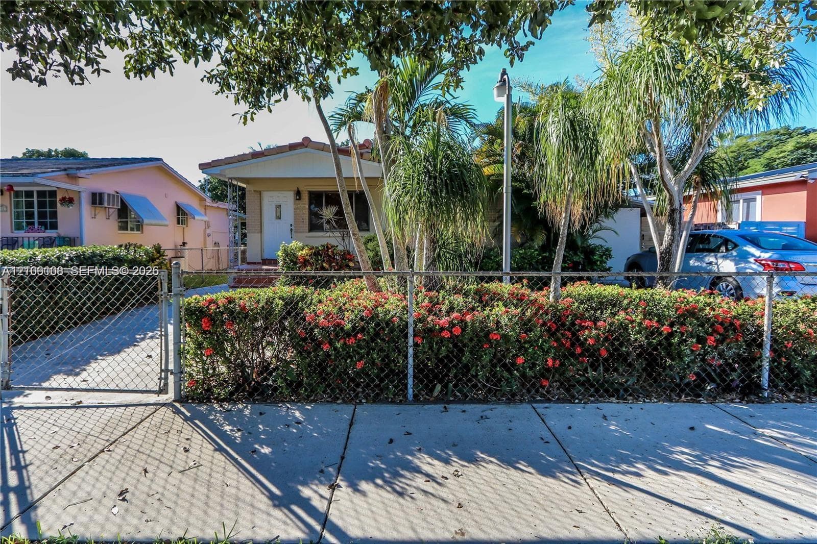 Single-story residence featuring a tile roof, covered front entrance, chain-link perimeter fencing, and mature tropical landscaping