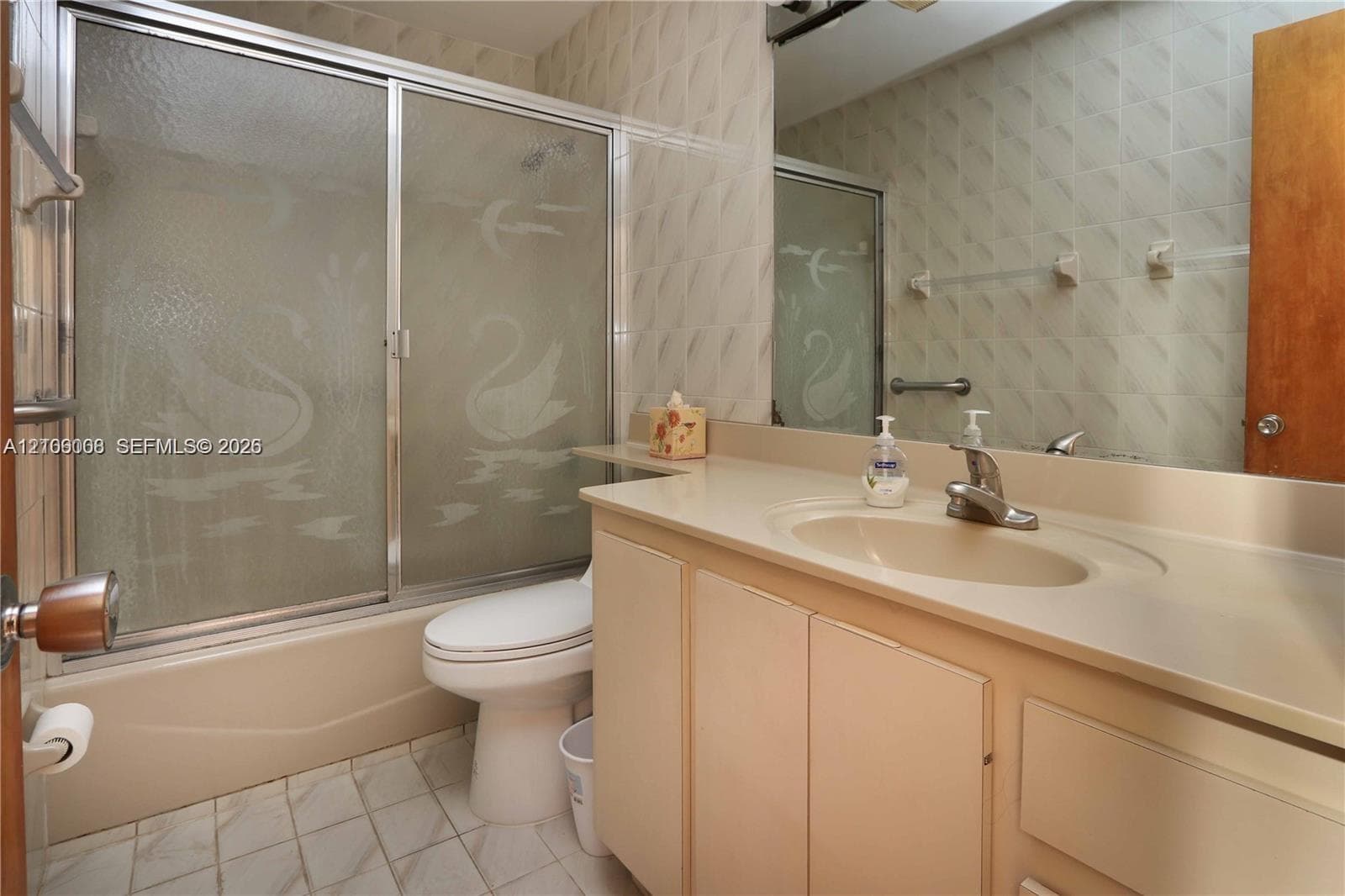 Bathroom featuring a vanity with an integrated basin, a combination shower and tub enclosure with sliding glass doors, and tile wall surfaces
