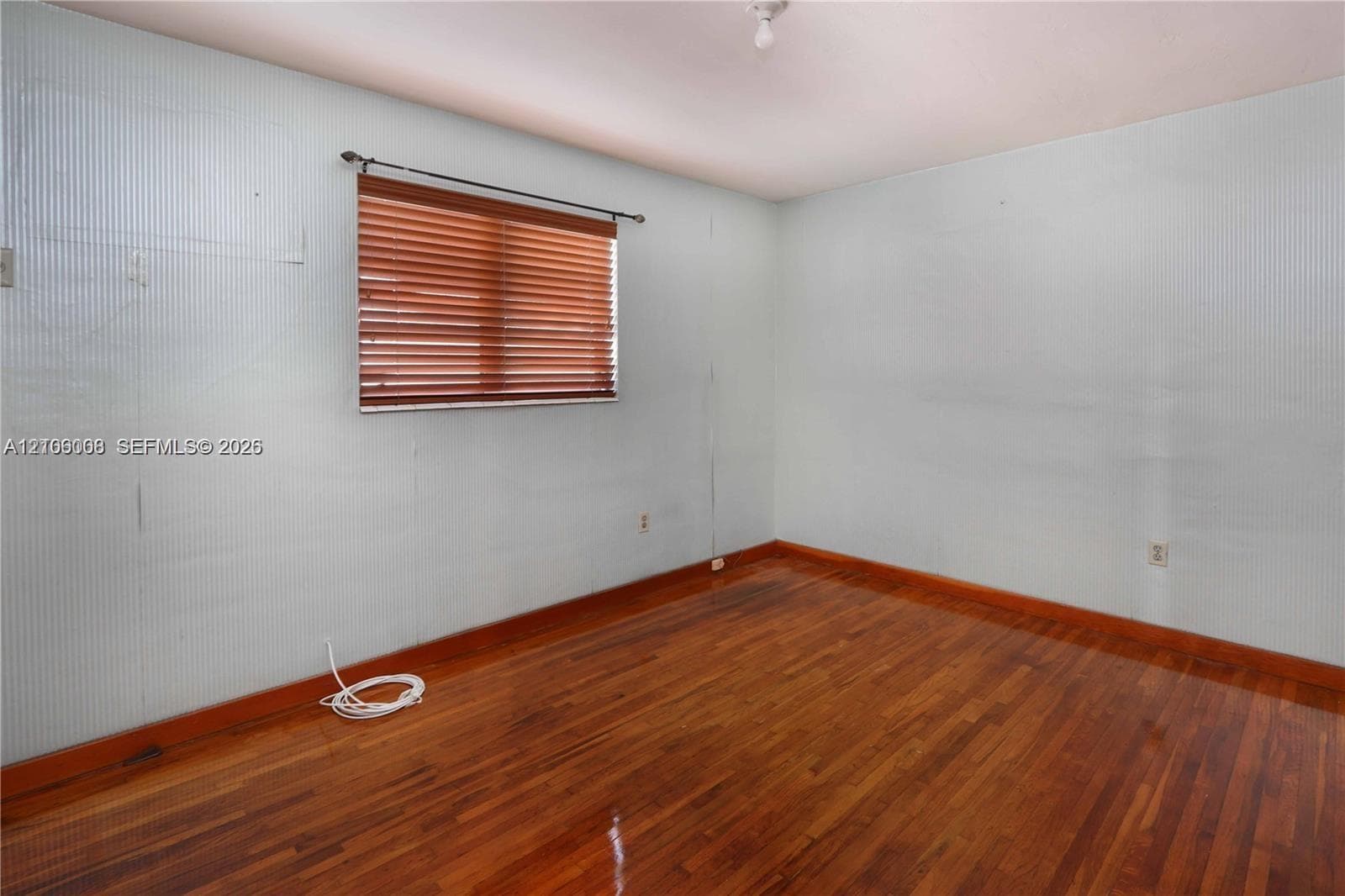 Room featuring wood-finish flooring, textured wall surfacing, and a window equipped with horizontal slat blinds