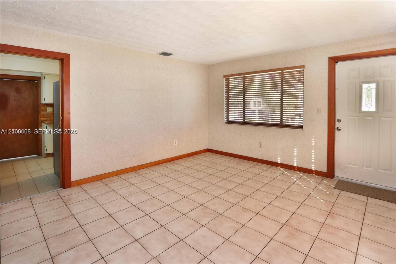 Interior space featuring neutral wall-to-wall ceramic tile flooring, a multi-pane window with horizontal blinds, and a paneled exterior door with an inset glass light