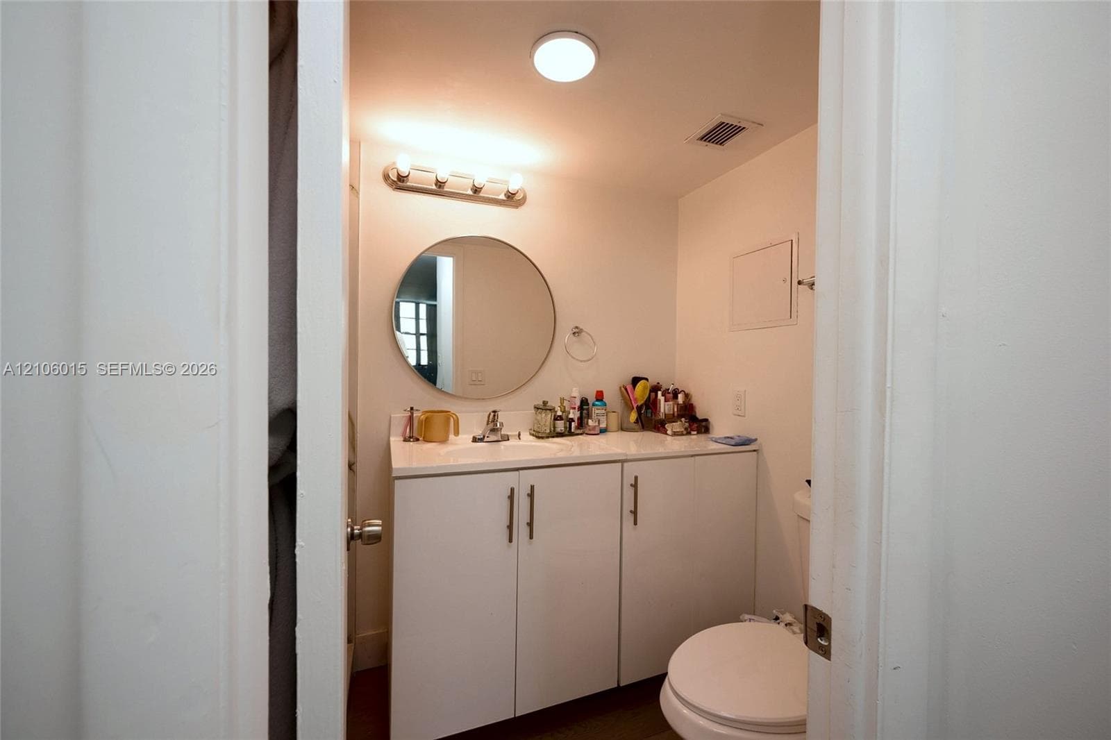 Bathroom vanity featuring white cabinetry, a solid-surface countertop with an integrated basin, a circular wall-mounted mirror, and a three-light fixture