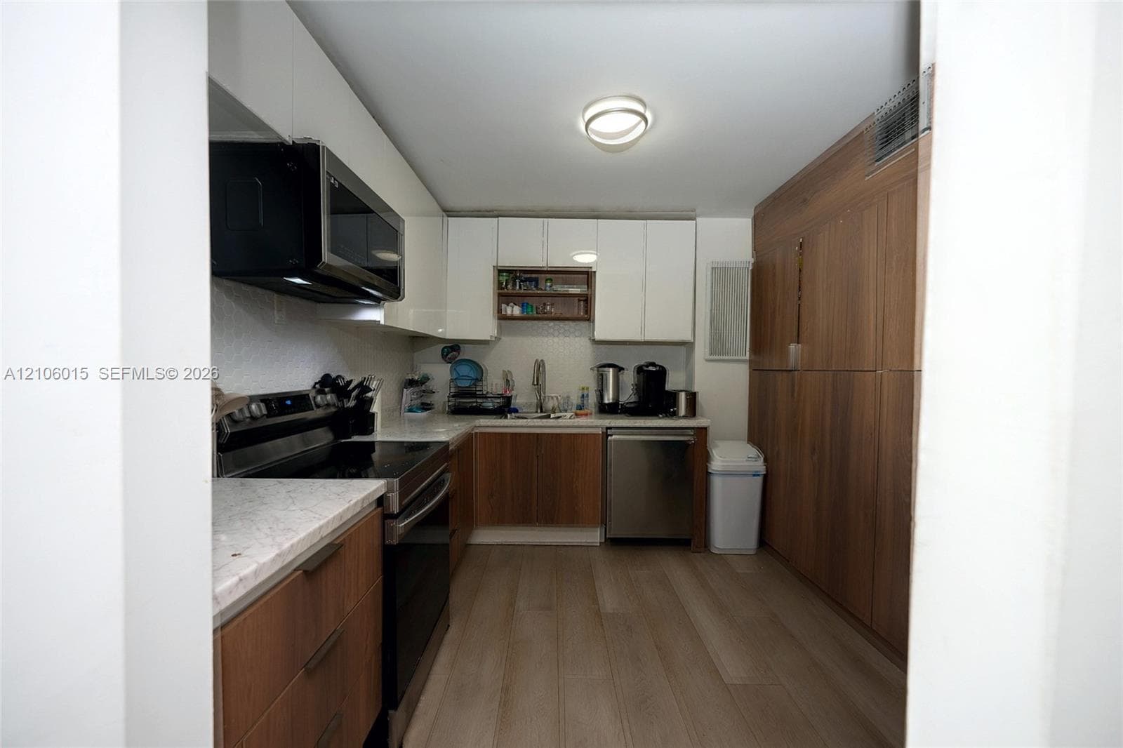 Kitchen featuring a combination of white upper cabinetry and wood-finish lower cabinetry, stone-finish countertops, stainless steel appliances, and wood-finish flooring