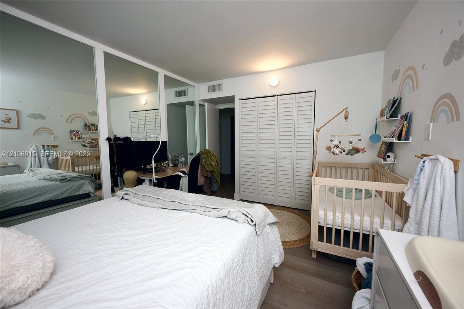 Bedroom featuring wood-finish flooring, floor-to-ceiling mirrored closet doors, white louvered-style closet doors, and wall-mounted shelving