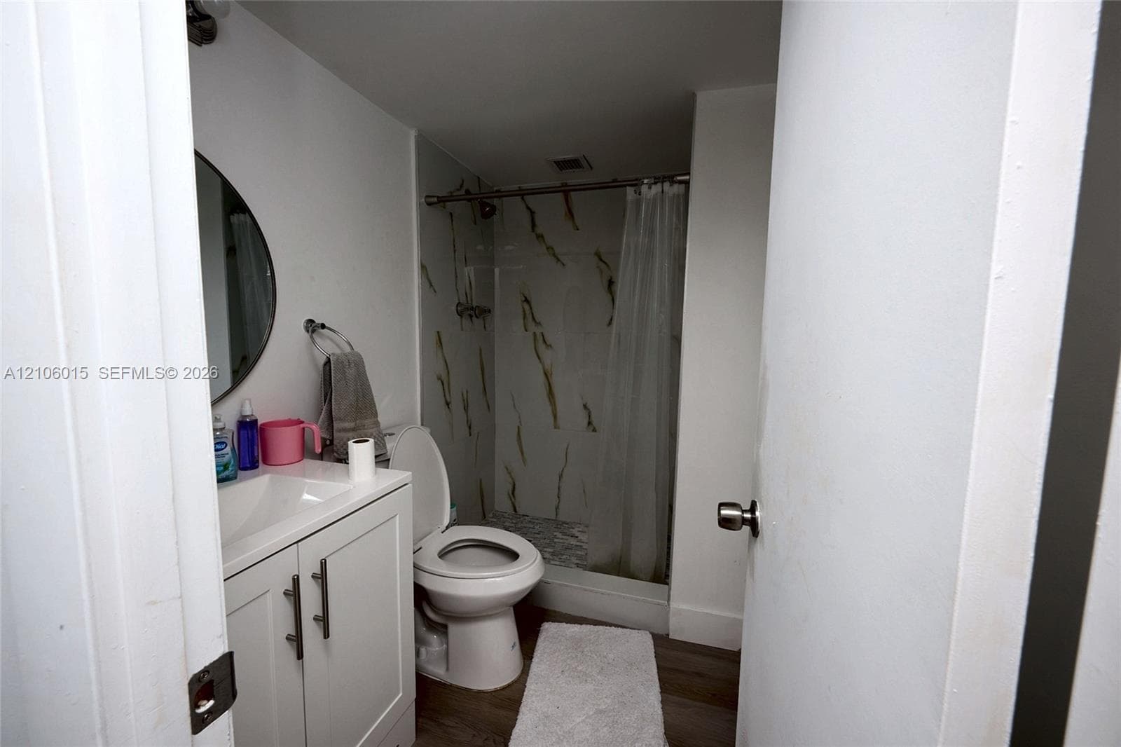 Bathroom featuring a white vanity cabinet, round wall mirror, and a tub-shower combination with patterned wall tile