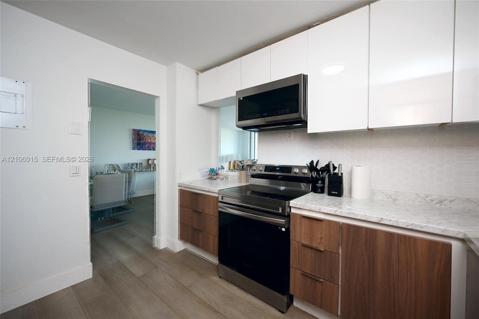 Kitchen featuring two-tone flat-panel cabinetry, light-toned stone-finish countertops, geometric tile backsplash, and stainless steel appliances
