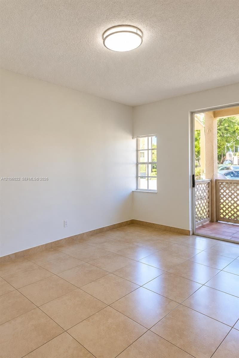 Neutral-toned ceramic tile flooring, flush-mount ceiling lighting, and glass sliding door access to a covered patio with lattice detailing