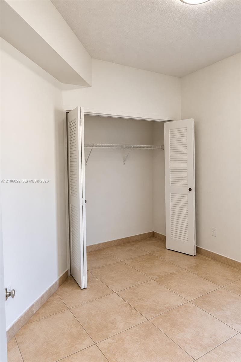 Neutral-toned ceramic tile flooring, walk-in closet with louvered bifold doors, and built-in wire shelving