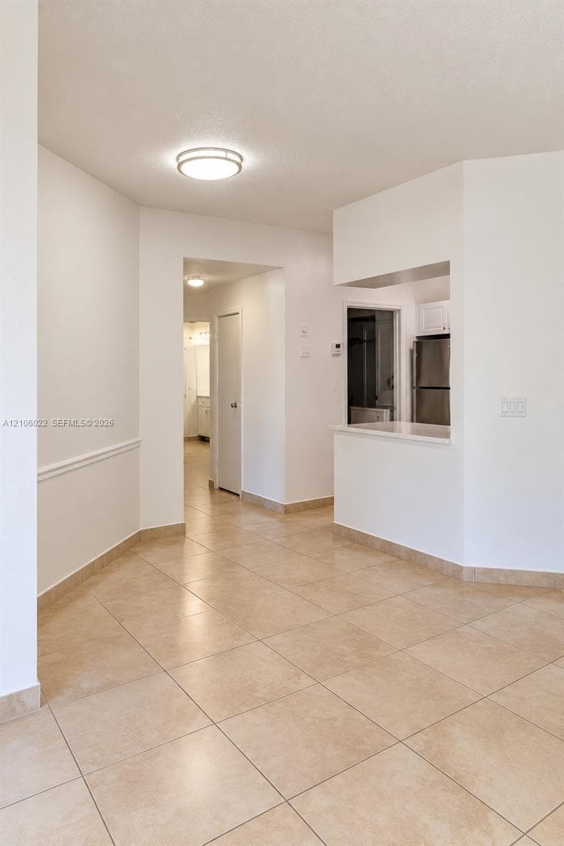 Interior space featuring large-format ceramic floor tiling, white walls, wainscoting detail, ceiling-mounted light fixtures, and a pass-through counter