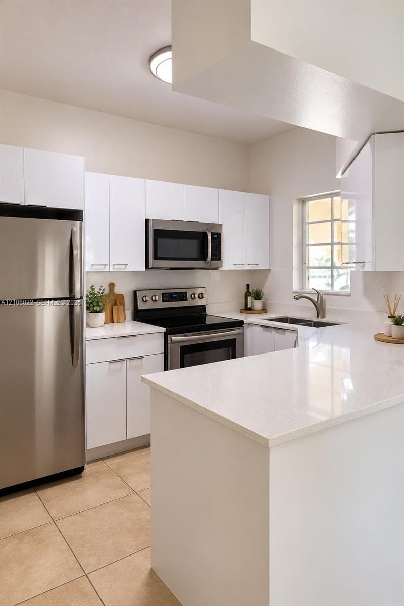Kitchen featuring high-gloss white cabinetry, quartz countertops, stainless steel appliances, dual-basin stainless steel sink, and large-format tile flooring