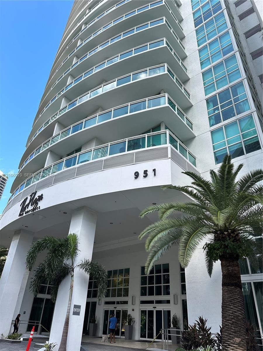 High-rise exterior featuring a curved white facade, multiple levels of glass-railed balconies, and floor-to-ceiling windows