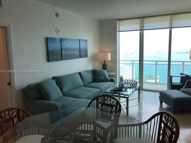 Floor-to-ceiling windows, light-toned stone flooring, and a glass-railed balcony overlooking the water