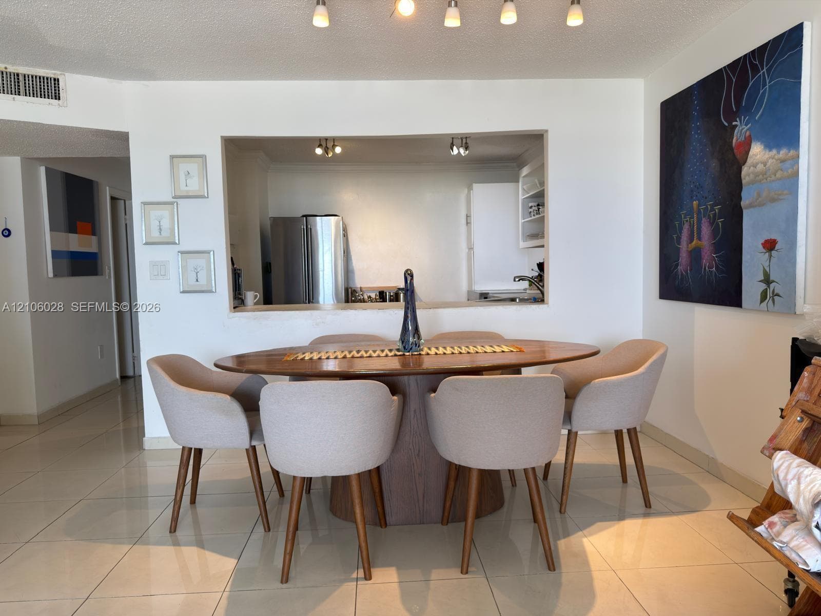 Interior space featuring neutral tile flooring, five-light track lighting, and a pass-through opening to the kitchen