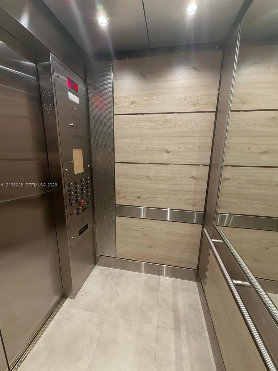 Elevator cab featuring wood-finish paneling, stainless steel trim, integrated mirror, brushed metal control panel, and recessed ceiling lighting