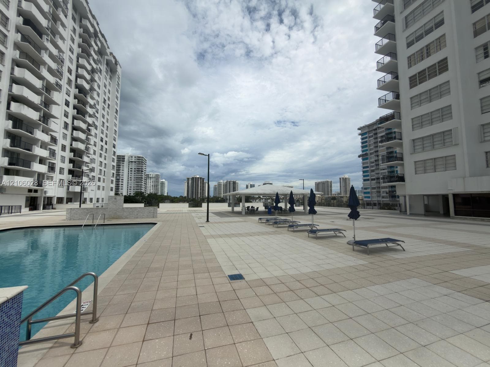 Outdoor pool with tiled surround, stone-clad water feature, and covered pavilion area