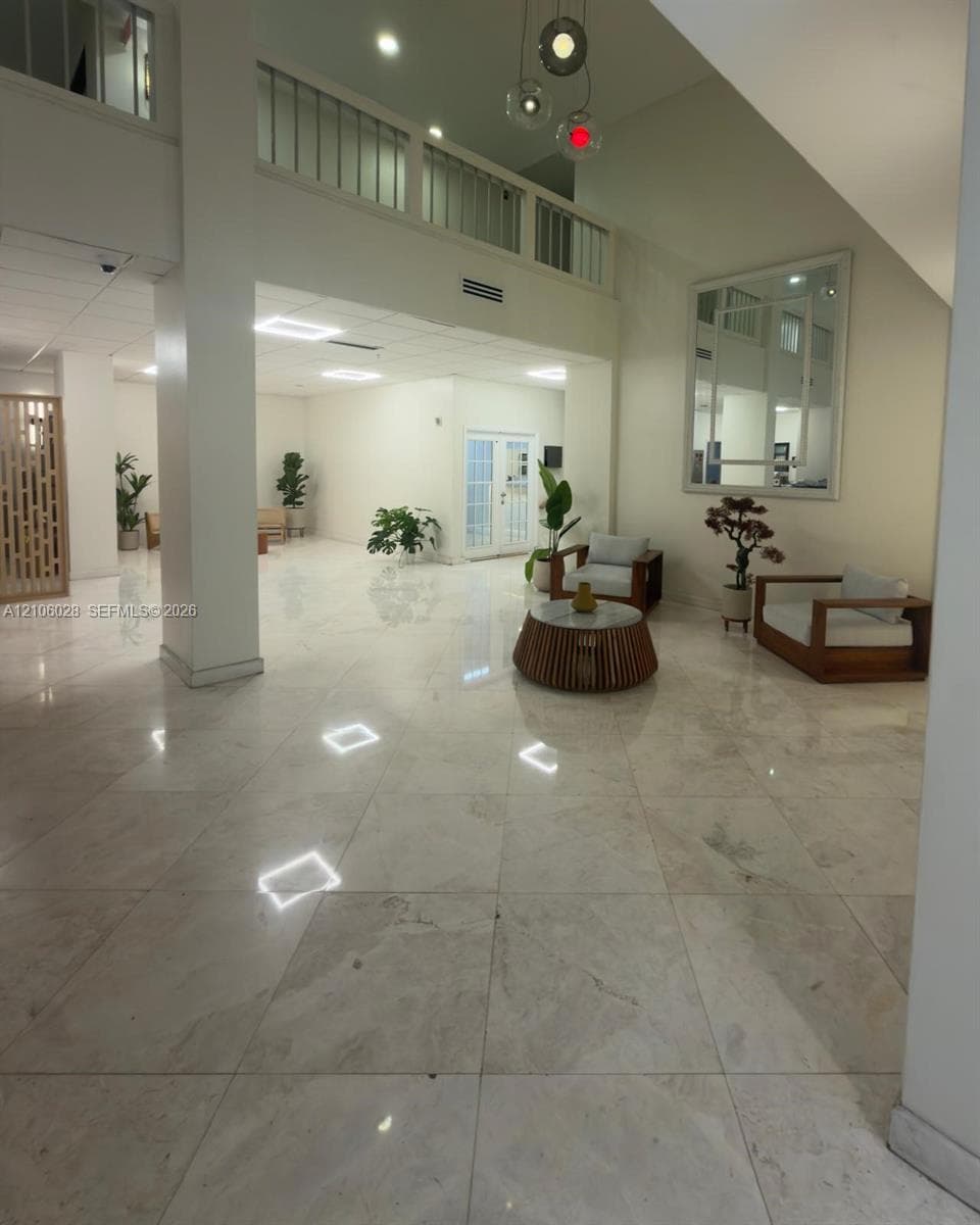Expansive foyer featuring polished stone flooring, vaulted ceilings, a structural support column, and a railed upper-level balcony