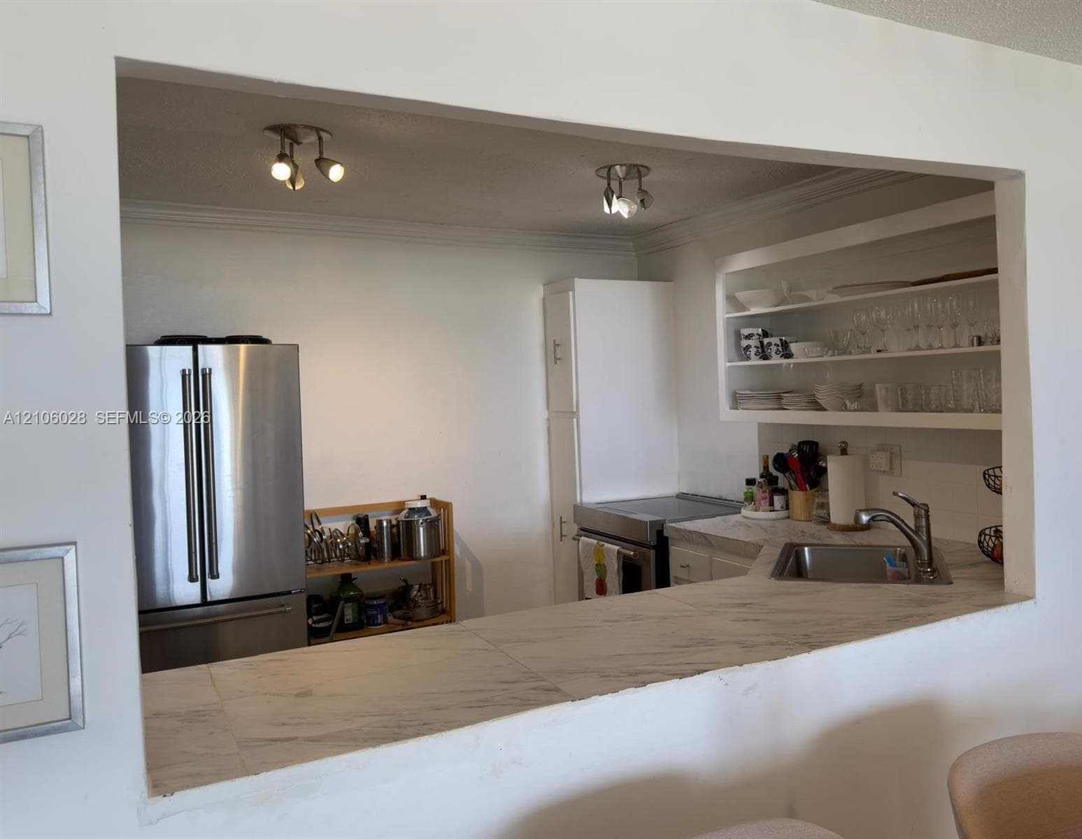Kitchen featuring a stone-surface pass-through counter, stainless steel refrigerator, built-in open shelving, and dual multi-directional track lighting