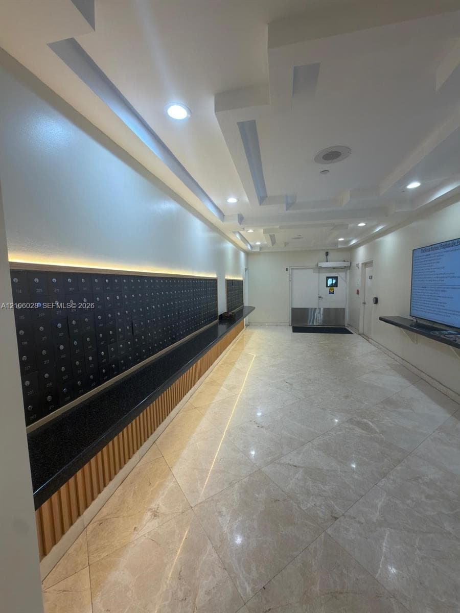 Communal mail area featuring stone tile flooring, recessed coffered ceilings with integrated lighting, wall-mounted mailboxes with a stone-finish counter, and vertical wood-slat accent detailing