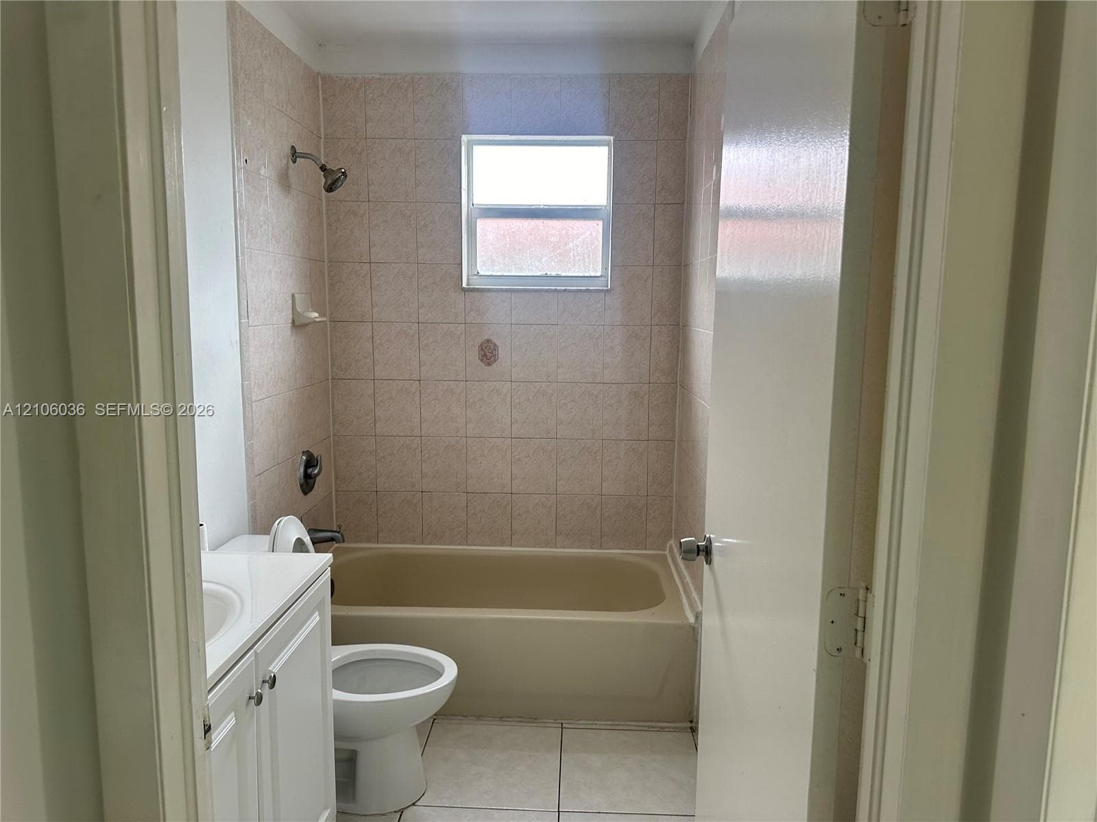 Bathroom featuring a white vanity cabinet, ceramic tile flooring, a tub-shower combination with tiled surround, and a window