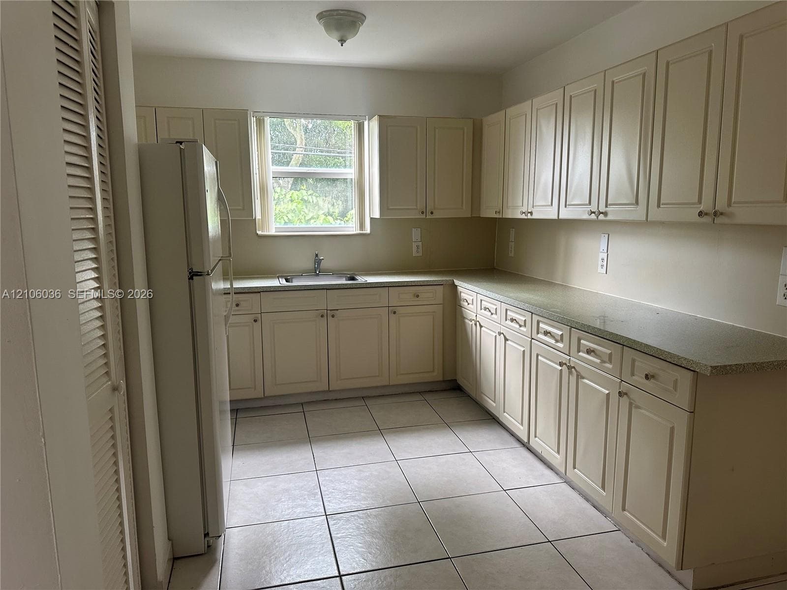 Kitchen featuring off-white cabinetry, solid-surface countertops, tile flooring, and a window above the sink