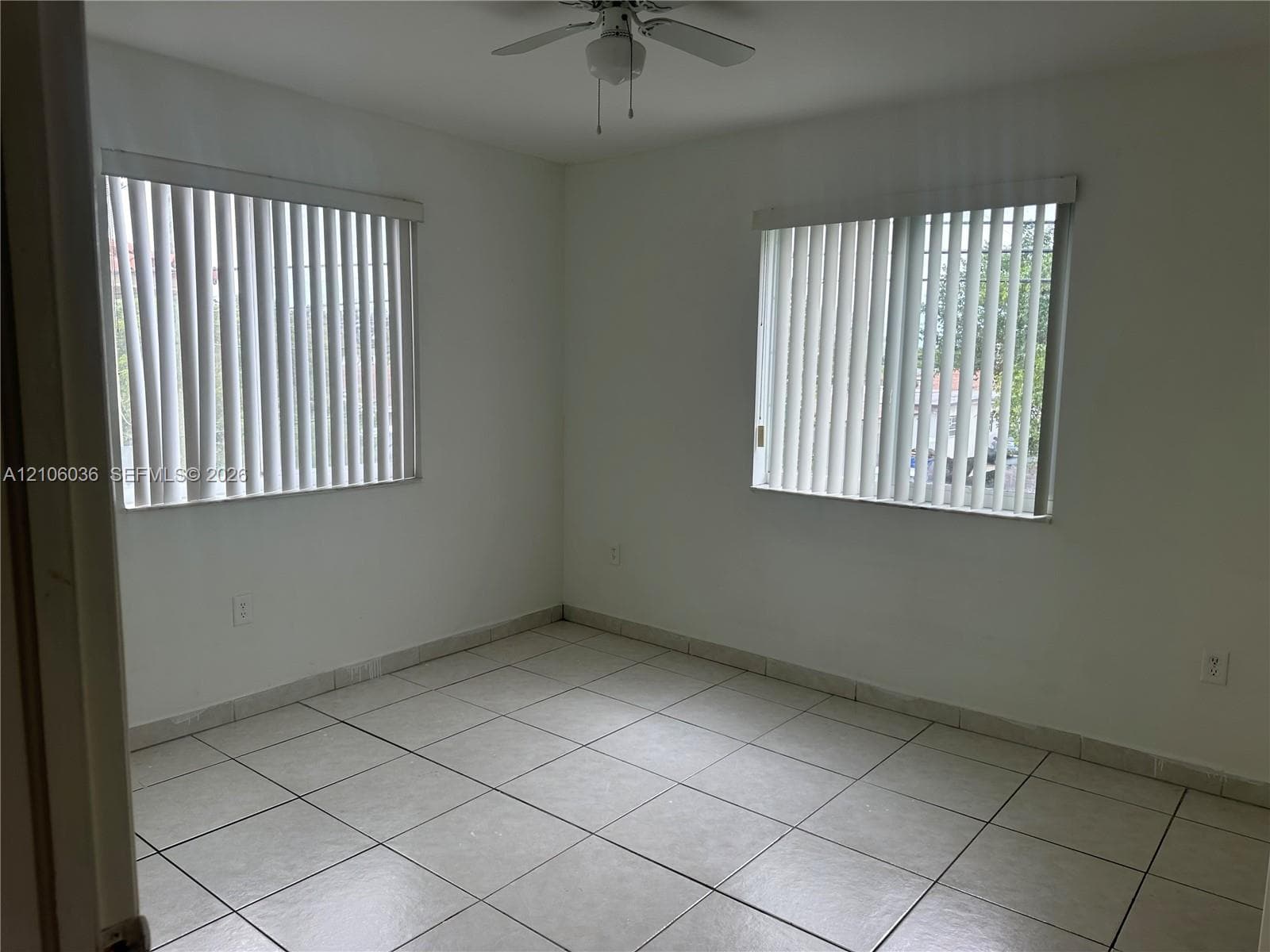 Neutral-toned tile flooring, dual windows with vertical blinds, and a ceiling fan with integrated lighting