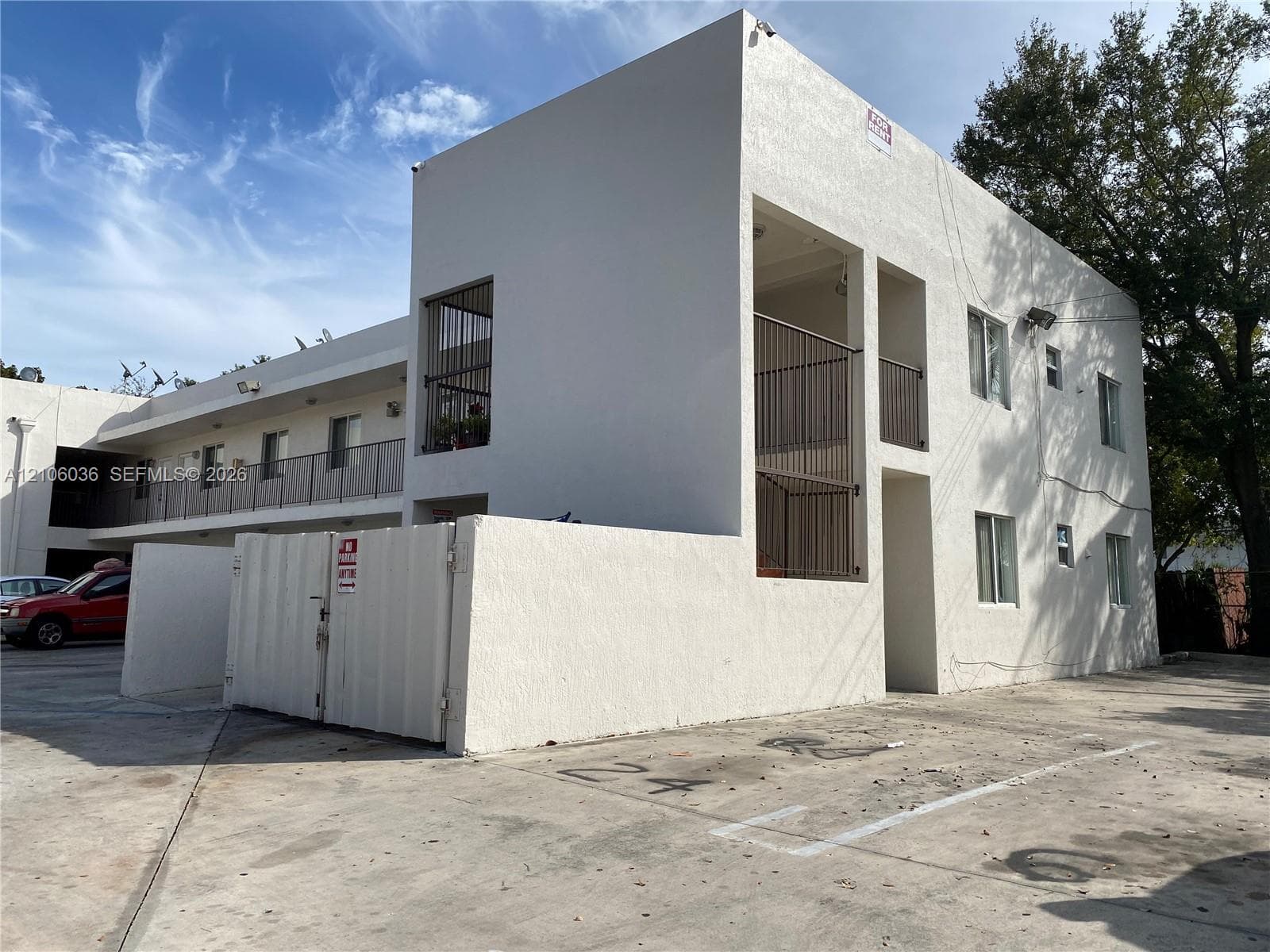 Multi-level structure featuring a stucco exterior, concrete-paved parking area, and metal-railed exterior stairwells and balconies