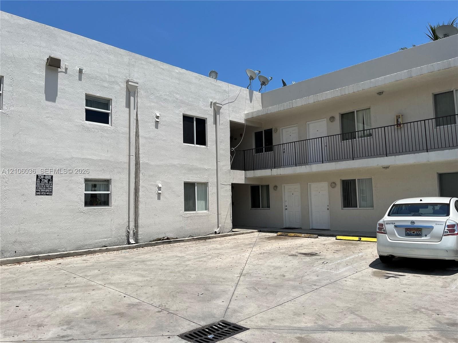 Two-story stucco exterior featuring a concrete parking area and an elevated walkway with metal railings