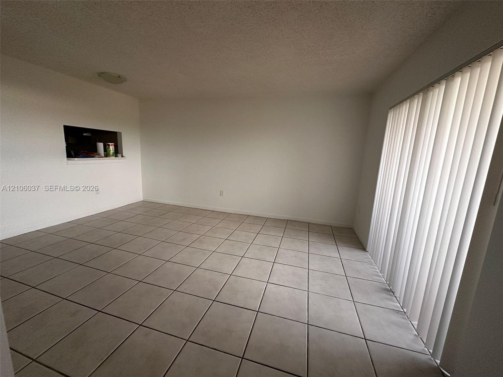 Room featuring neutral tile flooring, vertical window blinds, and a built-in wall pass-through