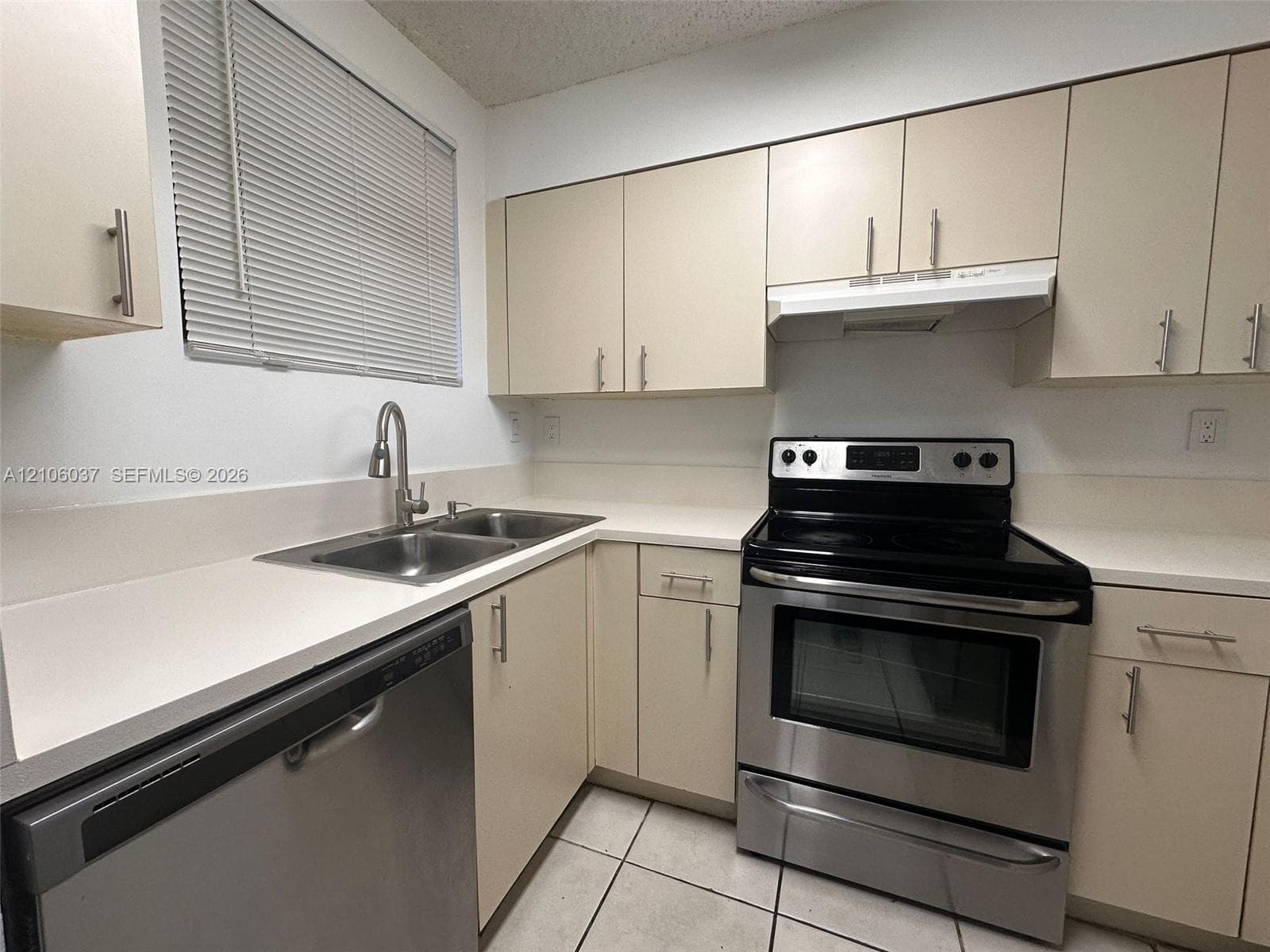 Kitchen featuring neutral flat-panel cabinetry, solid surface countertops, stainless steel appliances, a dual-basin sink with a gooseneck faucet, and tiled flooring