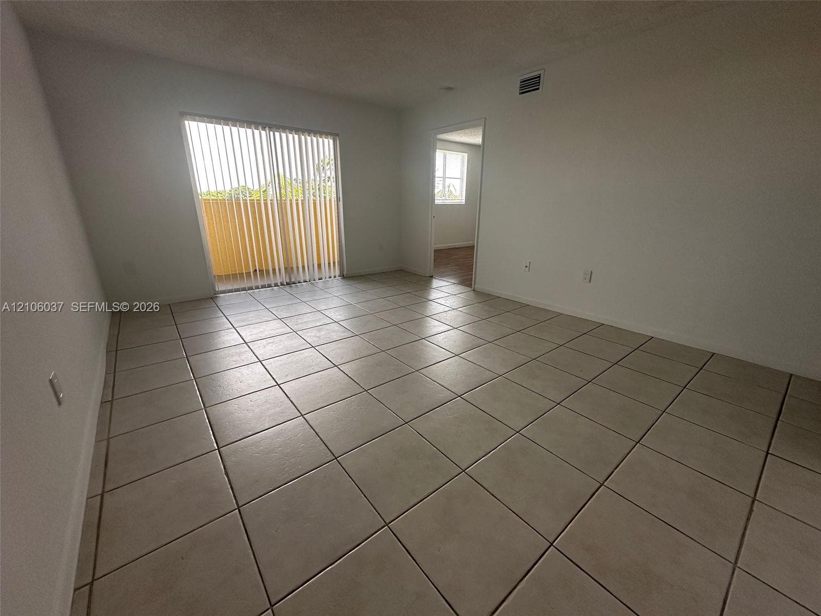 Interior room featuring large-format ceramic floor tile, sliding glass door with vertical blinds, and neutral wall tones