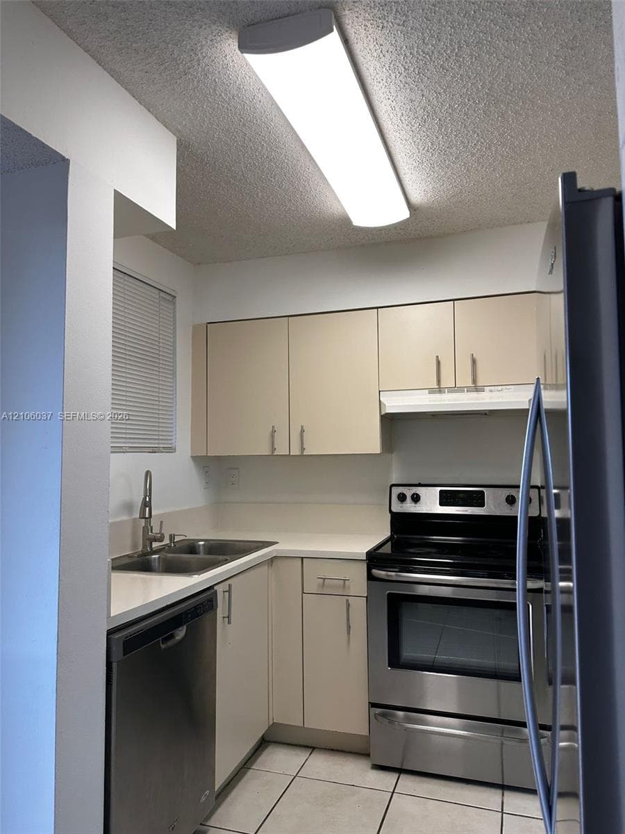 Kitchen featuring stainless steel appliances, double-basin sink with high-arc faucet, solid-surface countertops, flat-panel cabinetry, and tile flooring