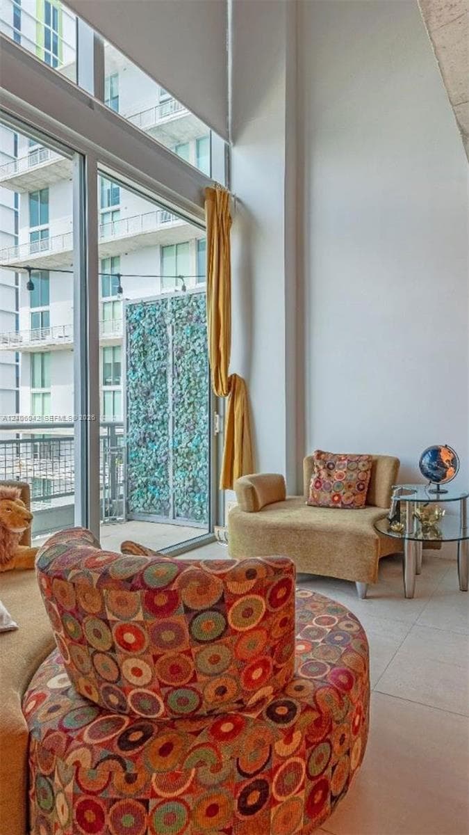 Floor-to-ceiling windows, high ceilings, neutral tile flooring, and a private balcony with metal railing