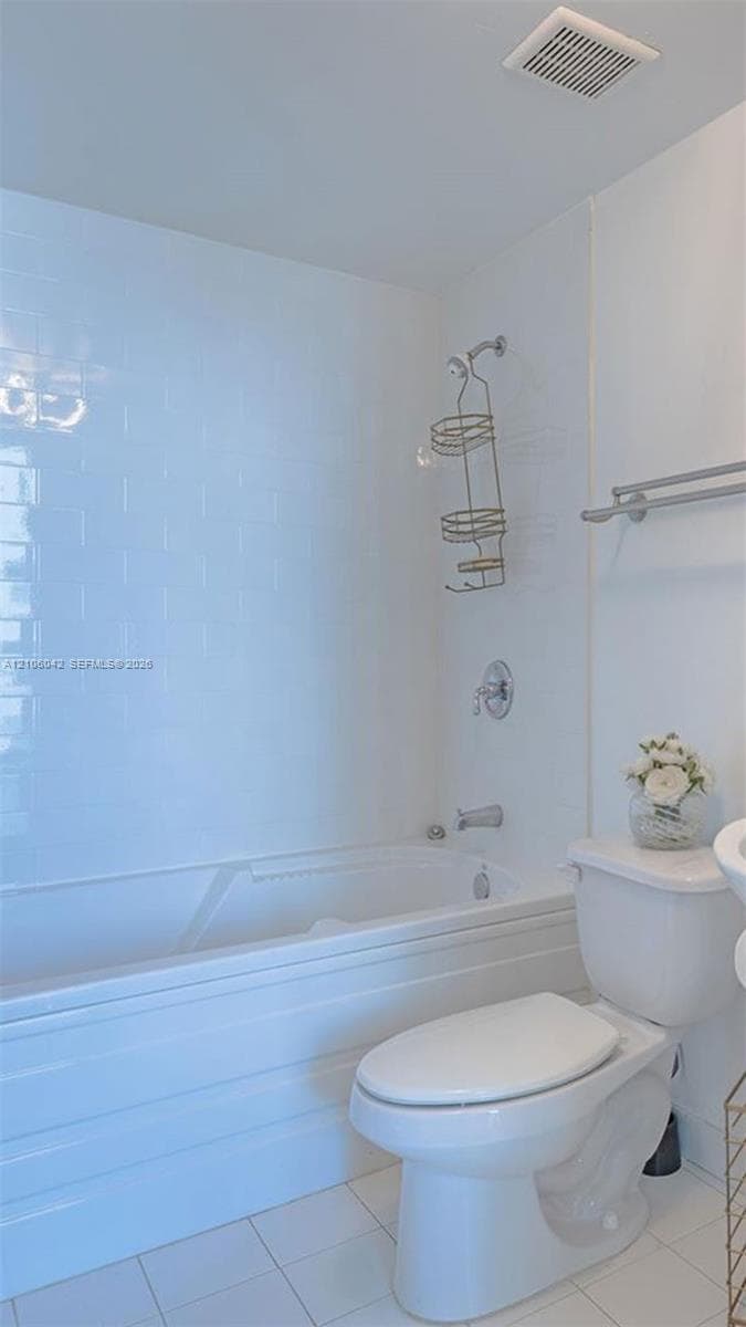 Bathroom featuring a white porcelain tub with tiled surround, chrome plumbing fixtures, and white tile flooring