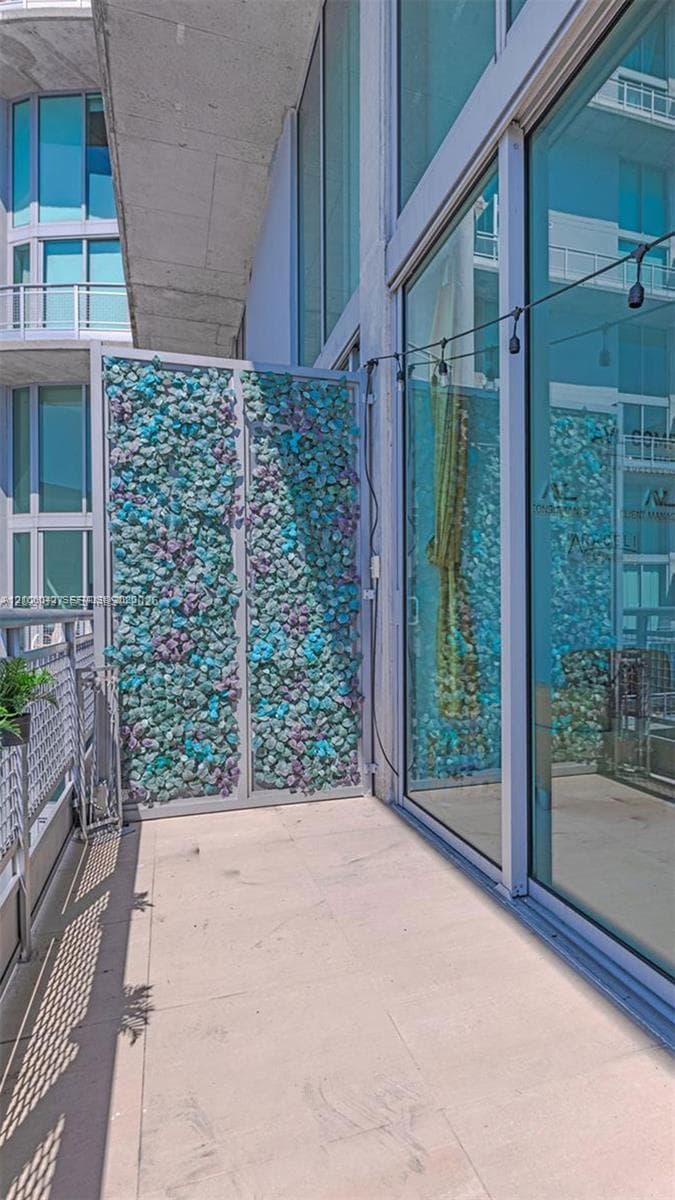 Private balcony featuring floor-to-ceiling glass paneling, concrete flooring, and a decorative privacy screen with integrated artificial foliage