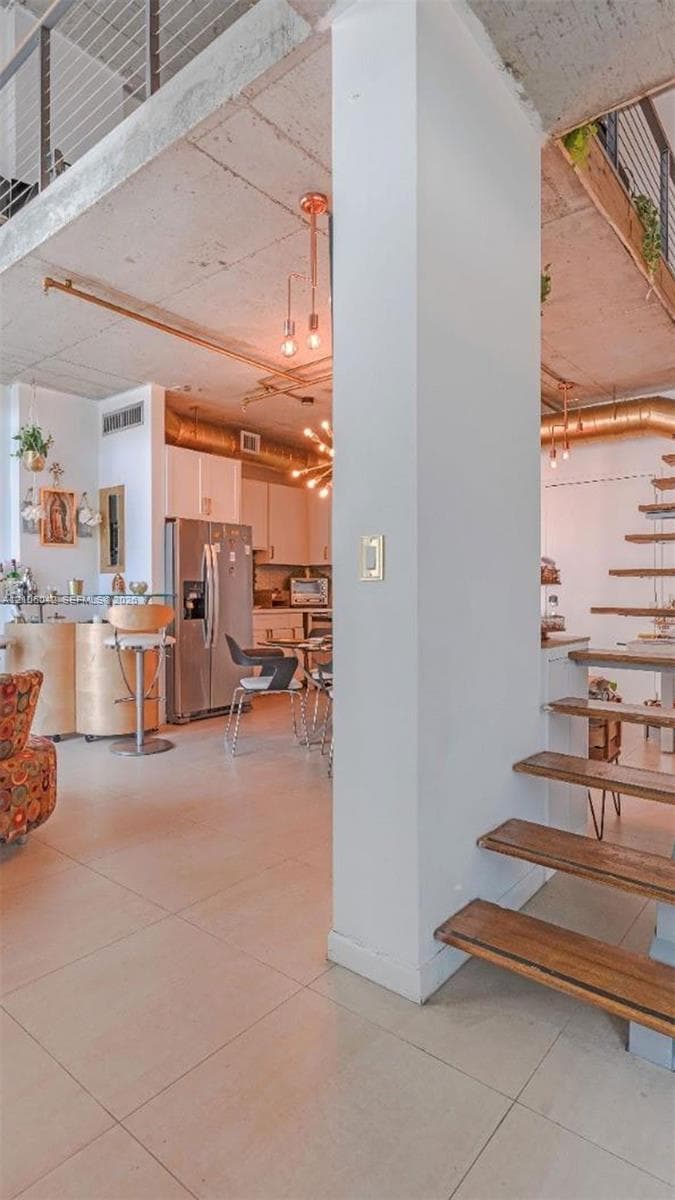 Open-concept interior featuring industrial concrete ceilings, exposed metallic ductwork, wood-tread floating staircase, and large-format tile flooring