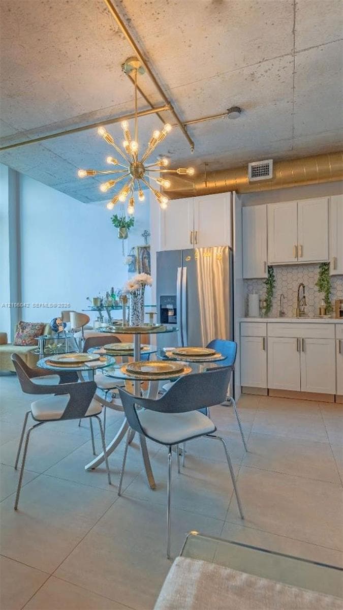 Exposed concrete ceiling with industrial-style ductwork, custom white cabinetry, starburst-inspired chandelier, and tile flooring