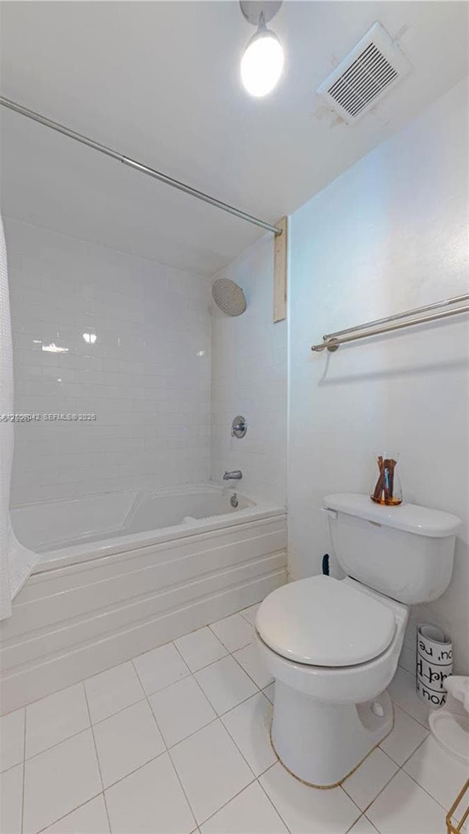 Clean and bright bathroom featuring white subway tile flooring, a white ceramic toilet with elongated bowl, and a bathtub-shower combination with frameless glass enclosure