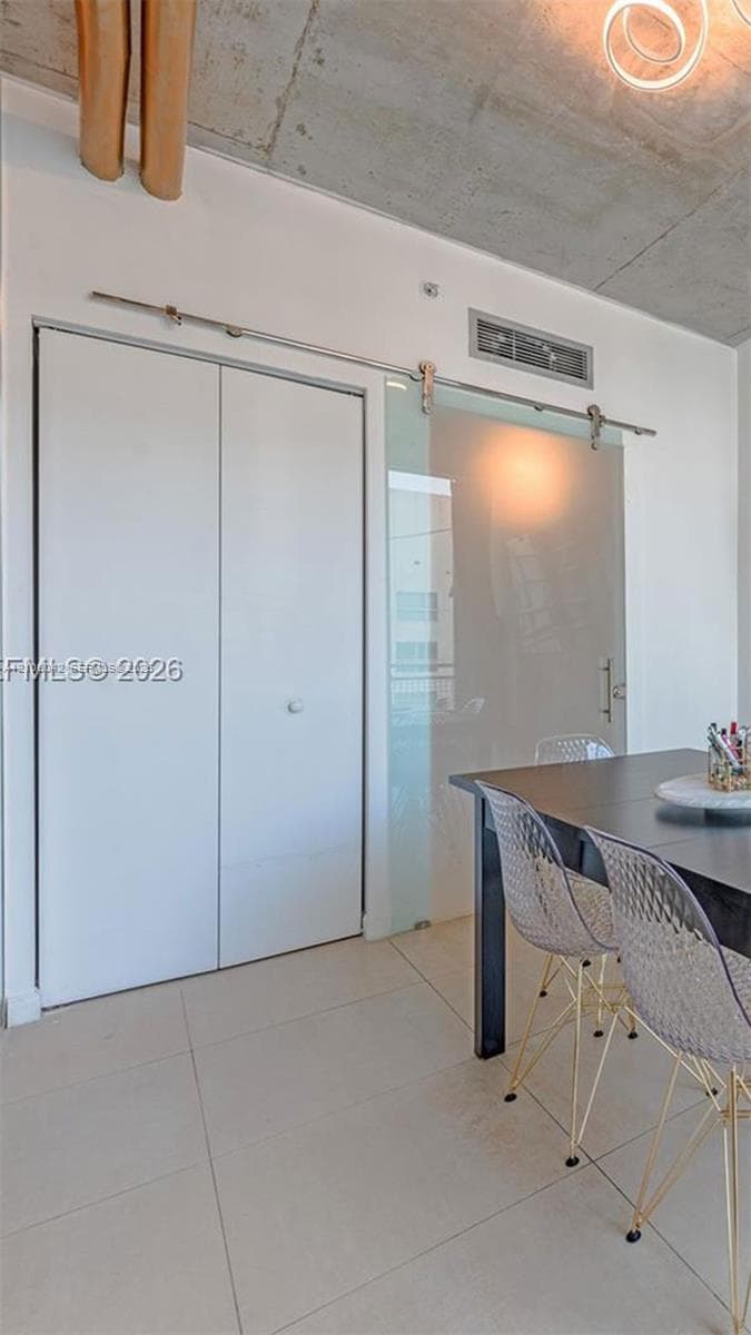 Exposed concrete ceiling, sliding frosted glass door with polished metal hardware, white dual-panel closet doors, and large-format tile flooring