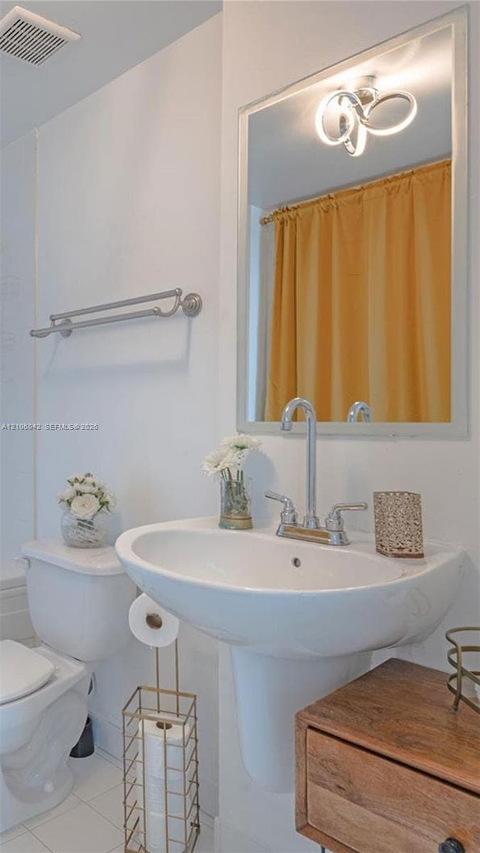 White pedestal sink with a chrome high-arc faucet, framed wall mirror, contemporary circular light fixture, and dual-arm towel bar