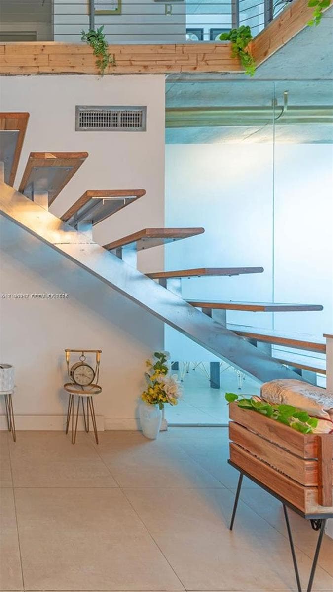 Open-riser staircase featuring metal stringers, wood-finish treads, and a cable railing system set against a polished tile floor