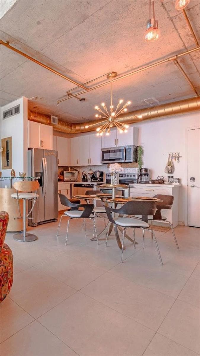 Industrial-style kitchen featuring exposed concrete ceilings, metallic ductwork, white cabinetry, tile flooring, and a multi-bulb Sputnik-style chandelier
