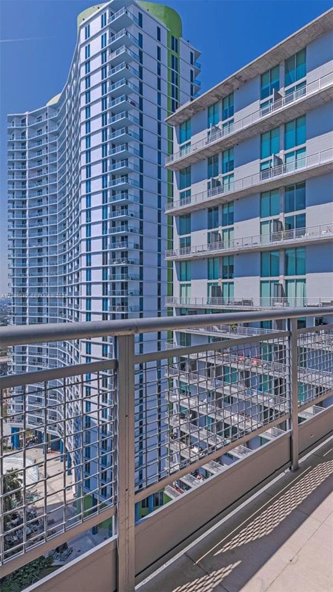 High-rise exterior featuring a concrete balcony with a metal mesh railing, tiered building design, and floor-to-ceiling glass windows