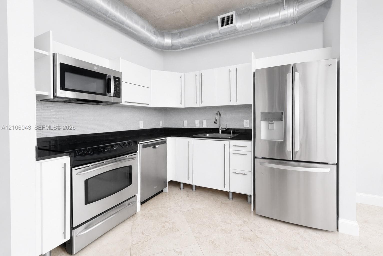Modern kitchen featuring flat-panel white cabinetry, contrasting black stone countertops, stainless steel appliances.